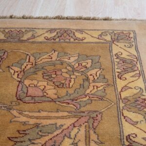 Medium-pile golden rug with intricate floral designs and visible fringe rests on light-colored wooden planks.