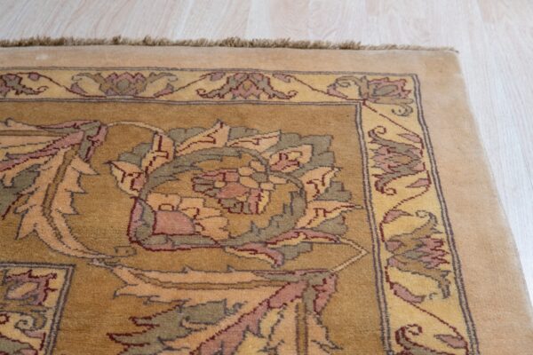 Medium-pile golden rug with intricate floral designs and visible fringe rests on light-colored wooden planks.