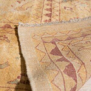 A low-pile yellow rug displaying red patterns is folded over on light wood flooring.