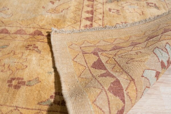 A low-pile yellow rug displaying red patterns is folded over on light wood flooring.