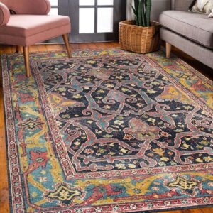 A navy, teal, and gold patterned rug anchors a pink armchair and gray sofa on shiny wood flooring.