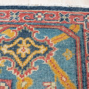 A blue, red, and yellow low-pile rug featuring a dense traditional geometric pattern on light wood floor.