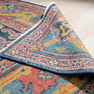 Blue, red, and gold patterned rug folded over light wood flooring, revealing its low-pile tight weave.