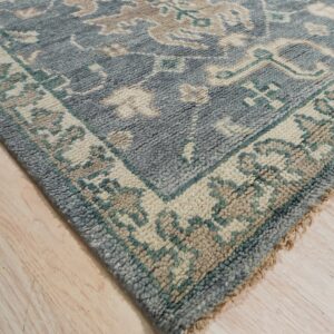 Textured slate-blue rug featuring cream and tan traditional patterns, displayed on light wooden floor.