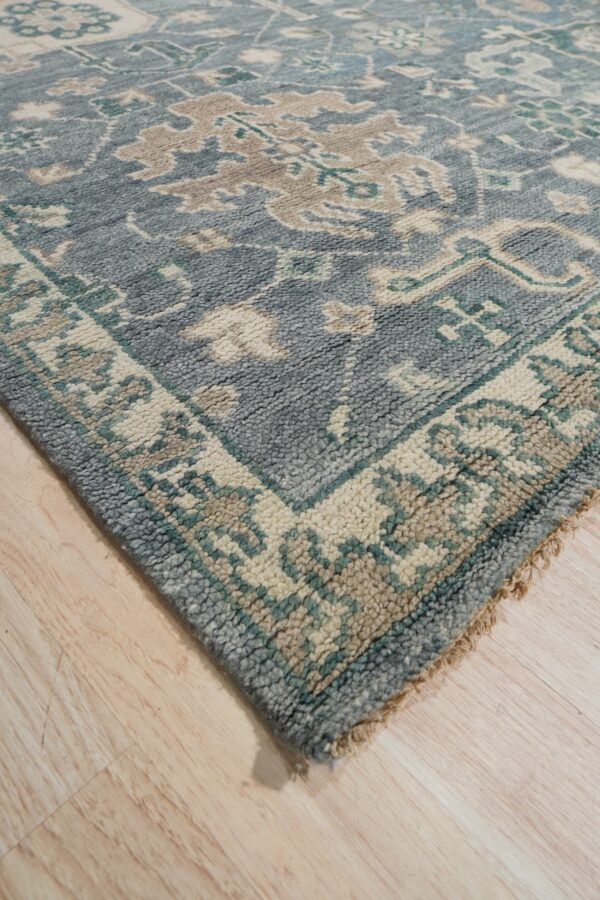 Textured slate-blue rug featuring cream and tan traditional patterns, displayed on light wooden floor.
