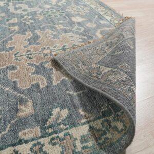 Blue, beige, and teal patterned rug with visible low pile rolled up on light wood flooring.