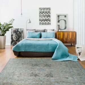 Distressed gray and teal traditional rug grounding a bedroom with a blue quilted bedspread and white walls.
