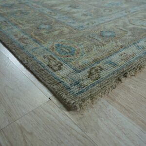 Textured beige rug corner with blue and yellow border patterns lying on light wood flooring.