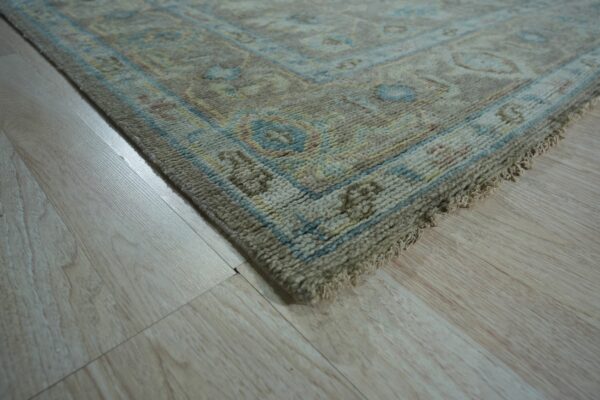 Textured beige rug corner with blue and yellow border patterns lying on light wood flooring.