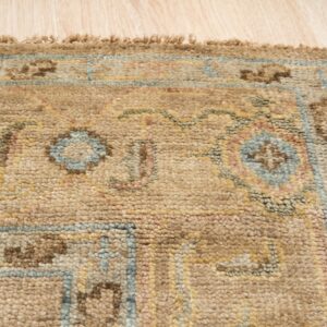 Chunky pile rug featuring muted tan, blue, and gold geometric patterns on light wood flooring.