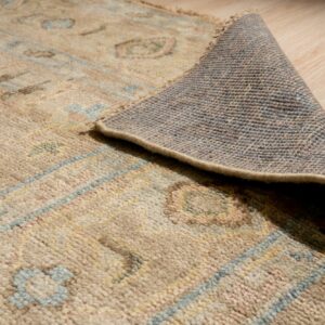Muted beige rug with abstract blue and pink patterns peeled back, revealing the backing on wood planks.