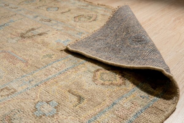 Muted beige rug with abstract blue and pink patterns peeled back, revealing the backing on wood planks.