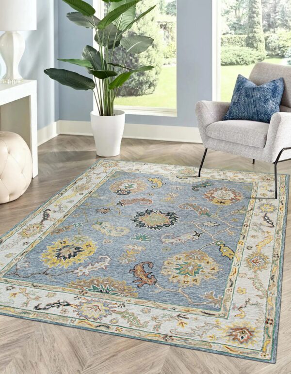 Traditional blue and gold area rug featuring an ornate border placed beneath a gray upholstered chair.