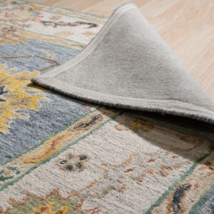 A high-pile rug with blue, cream, and yellow traditional patterns is curled back, showing its gray backing on light wood floor.