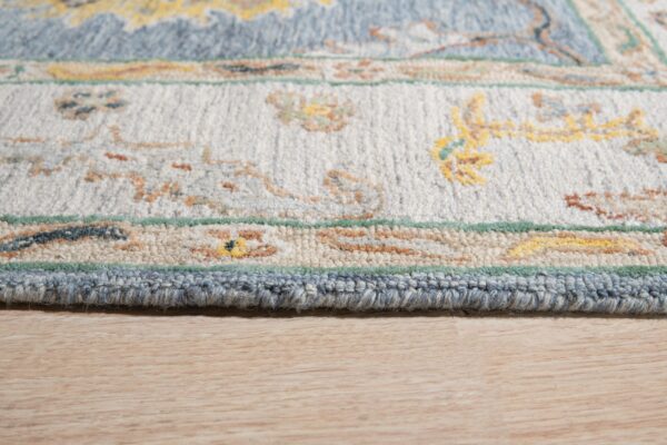 Detail of a plush rug featuring blue, cream, and yellow ornate patterns on light wood flooring.