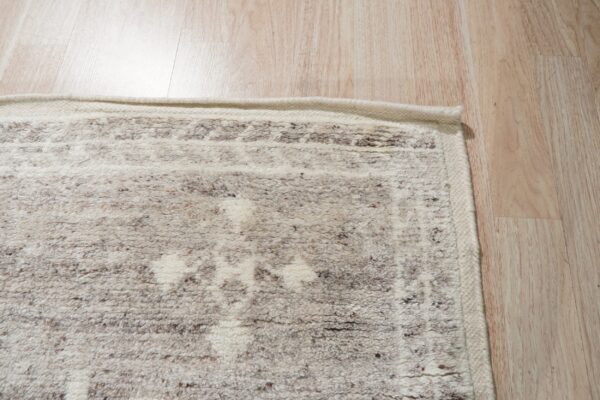 Close-up of a shaggy off-white and brown patterned rug edge on light wood plank flooring.