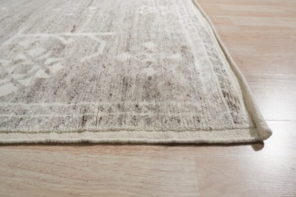 Textured cream and brown patterned rug edge shown close-up on light wood plank flooring.