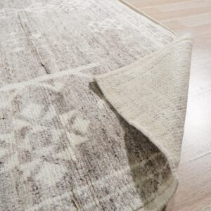 A textured off-white rug with brown speckling is peeled back on light wood plank flooring.
