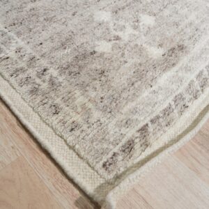 Textural off-white rug with brown flecks and subtle patterning rests on light blonde plank flooring.