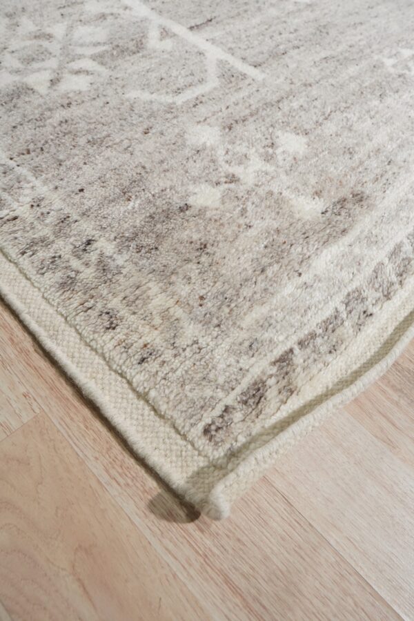 Textural off-white rug with brown flecks and subtle patterning rests on light blonde plank flooring.