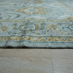 Thick textured rug in pale blue, gold, and teal on light wood flooring.