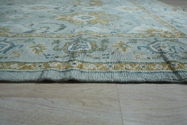 Thick textured rug in pale blue, gold, and teal on light wood flooring.