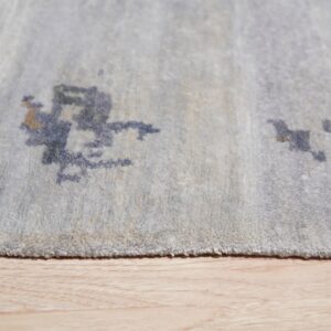Close detail of a pale blue rug with dark abstract patterns resting on light wood flooring.