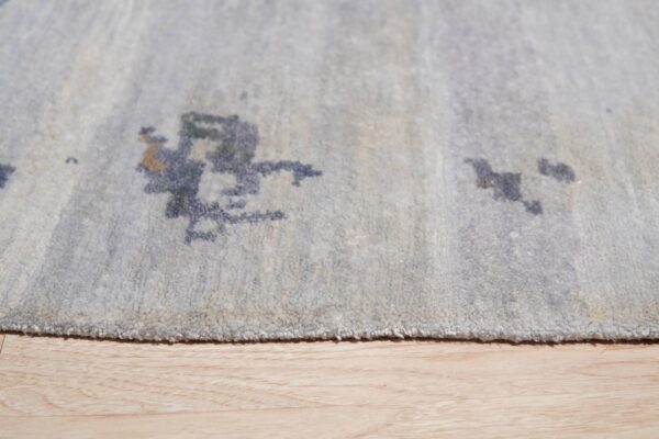 Close detail of a pale blue rug with dark abstract patterns resting on light wood flooring.