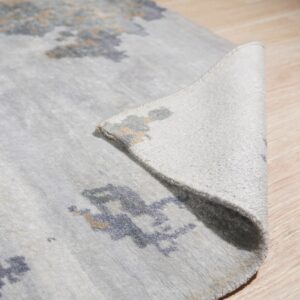Abstract blue and beige patterns accent a light gray rug partially curled on a light wood floor.