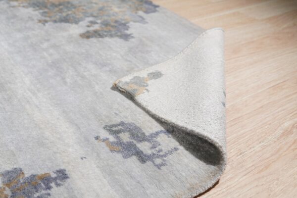Abstract blue and beige patterns accent a light gray rug partially curled on a light wood floor.