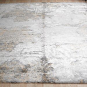Distressed silver, gold, and gray abstract rug with a low pile sheen sits on light hardwood.