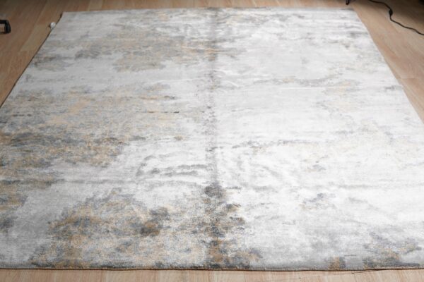 Distressed silver, gold, and gray abstract rug with a low pile sheen sits on light hardwood.