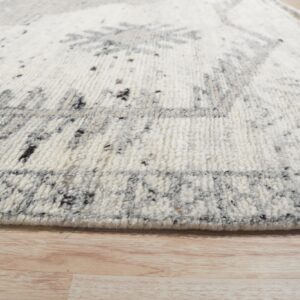 Textured, cream-colored rug with gray abstract motifs and speckling rests on light wooden flooring.