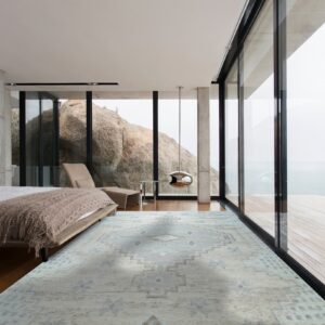A low-pile gray and light blue geometric rug grounds a modern bedroom with concrete walls and window views.