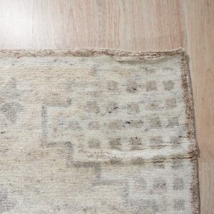 High-pile ivory rug with a chunky taupe geometric pattern lies on light wood flooring.