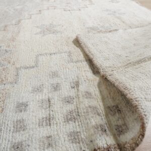 Textured off-white rug with geometric brown and gray patterns, shown folded on light wood floor.