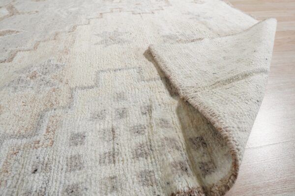 Textured off-white rug with geometric brown and gray patterns, shown folded on light wood floor.