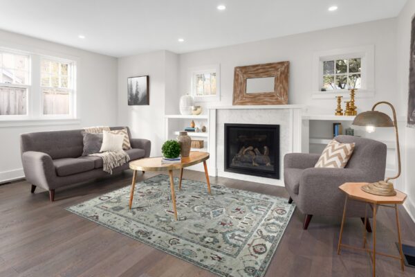A distressed sage green area rug with traditional patterns anchors a neutral living room with dark wood floors.