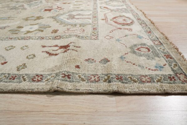 Textured cream rug with traditional medallions and borders in rust and sage on pale wood planks.