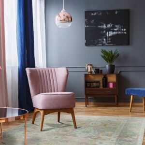Muted pink and green distressed traditional rug on a wood floor under a blush pink chair.