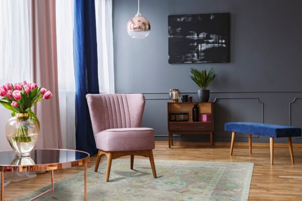 Muted pink and green distressed traditional rug on a wood floor under a blush pink chair.