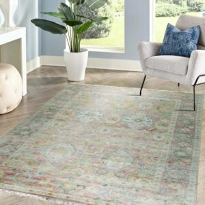 Muted pink and teal traditional patterned rug on herringbone wood flooring next to a gray armchair.