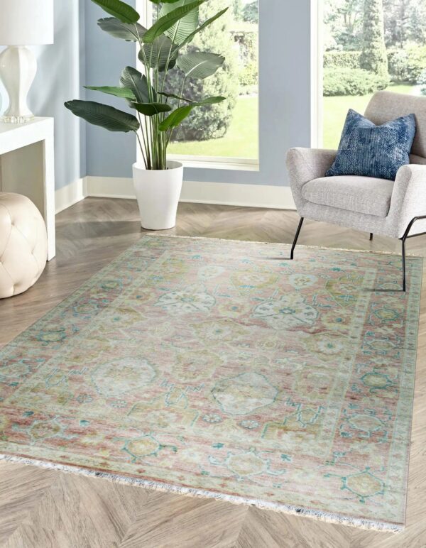 Muted pink and teal traditional patterned rug on herringbone wood flooring next to a gray armchair.