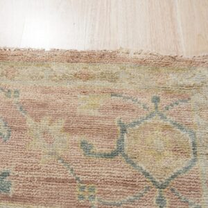 Textured rug detail featuring rose, cream, and gray-blue traditional patterns on light wood flooring.