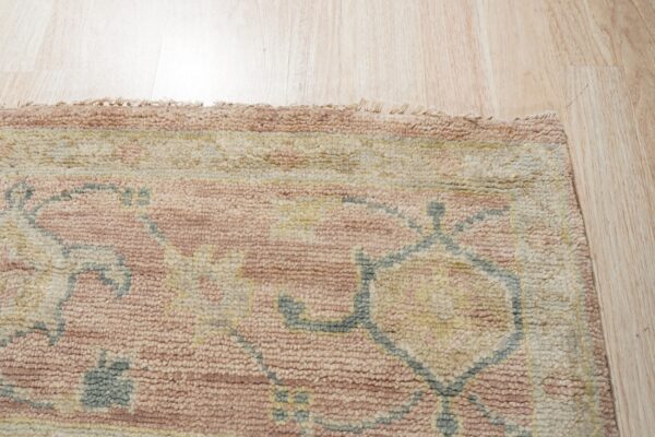 Textured rug detail featuring rose, cream, and gray-blue traditional patterns on light wood flooring.