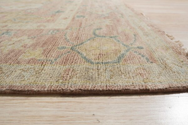 Angled view of a medium pile rug featuring rosy pink, cream, and blue designs on blonde wood flooring.