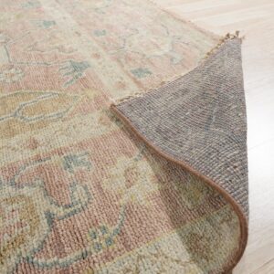 Low pile pink, cream, and tan patterned rug partially rolled to reveal the backing on light wood floors.