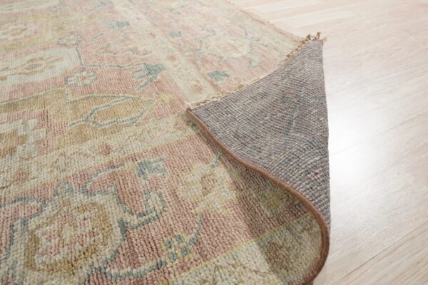 Low pile pink, cream, and tan patterned rug partially rolled to reveal the backing on light wood floors.