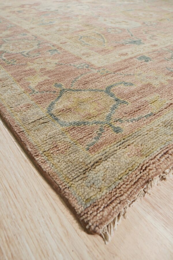 Chunky pile rug in rose, beige, and blue-gray geometric patterns resting on light wood flooring.