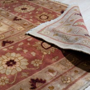A high-pile beige and dusty rose rug with a floral pattern is rolled back on light wood flooring.